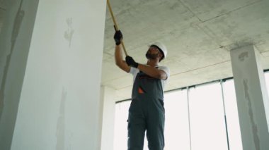 Tulum ve koruyucu giysili bir inşaat işçisi binanın içinde inşaat halindeki bir duvarı boyuyor.