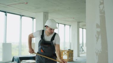 Bir müteahhit, inşaat alanındaki bir silindiri kullanarak duvara dikkatlice bir bitiş çizgisi uyguluyor. Güvenlik kıyafeti giyiyor.