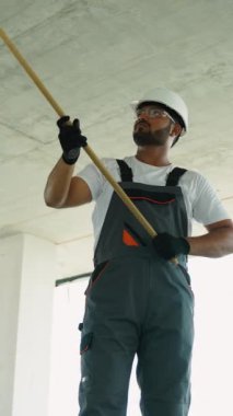 Tulum ve koruyucu giysili bir inşaat işçisi binanın içinde inşaat halindeki bir duvarı boyuyor.