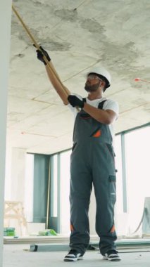 Hintli inşaat işçisi bir inşaat alanında paten kullanarak duvarları kaplarken ya da bitirirken görülüyor. Kask ve eldiven giymişti.