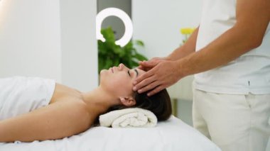 Profesyonel bir terapist, huzurlu bir spa ortamında bir kadına sakinleştirici bir kafa masajı sağlar. Tedavi stresi azaltmaya, gerilimi azaltmaya ve genel rahatlama ve refahı arttırmaya yardımcı olur.
