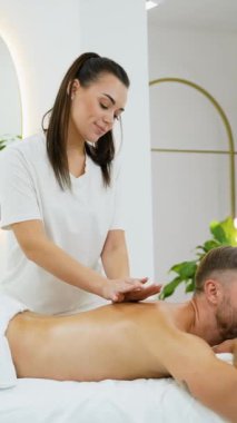 Erkek bir müşteri, huzurlu bir kaplıcada boyun masajı yaptırır. Terapist boyun gerilimini hafifletmek ve rahatlamayı teşvik etmek, genel refahı ve rahatlığı arttırmak için nazik bir baskı uyguluyor.