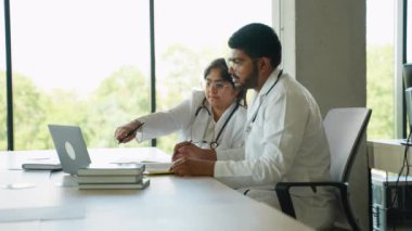 İki Hintli tıp stajyeri bir üniversite sınıfında çalışmalarına odaklanmış durumdalar. Bir dizüstü bilgisayar ve ders kitabı kullanıyorlar, klinik görevlere hazırlanırken tıbbi kavramları aktif olarak tartışıyorlar ve