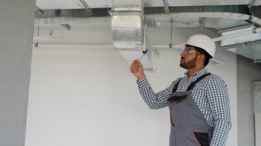 Hintli teknisyen bir ofis binasına havalandırma sistemi kuruyor. Bu fotoğraf, uygun hava dolaşımı ve güvenliği için havalandırma sistemi kurulumu ve bakımı kavramını temsil etmektedir.
