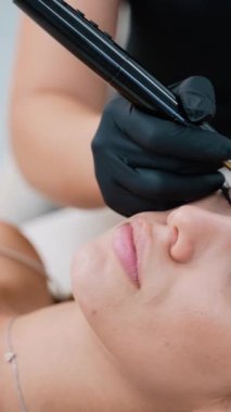 Yetenekli bir makyaj sanatçısı kusursuz bir estetik dövme prosedürü uygular. Müşteri rahatlarken, teknisyen siyah eldiven giyip detaylara ve hijyenik uygulamalara dikkat ediyor.