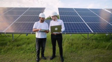 Hintli ve Avrupalı bir mühendis bir dizüstü bilgisayar kullanarak güneş paneli performansını tartışıyor. Yenilenebilir enerji çözümlerinin verimliliğini artırmak için işbirliği yapıyorlar