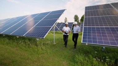 İki mühendis, bir Hintli ve bir Kafkasyalı güneş enerjisi çiftliğinde yan yana yürüyorlar. Sert şapkalar takarak güneş enerjisi performansını tartışırken güneş panellerini dizüstü bilgisayarla inceliyorlar.