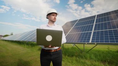 Avrupalı mühendis güneş panelleri önünde dizüstü bilgisayarla duruyor, enerji üretim verilerini ve sistem performansını değerlendiriyor. Bu, yenilenebilir enerji projelerinde teknolojinin rolünü vurgular