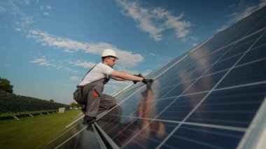 Bir işçi güneş panellerini dikkatlice güneş çiftliğinde matkap kullanarak güvence altına alıyor. Bu resim, yenilenebilir enerji projelerinde güneş enerjisi sistemlerinin korunması için gereken teknik becerileri vurgular