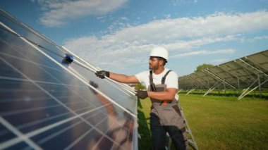 Üniformalı Hintli işçi güneşli bir günde güneş panellerini temizleme aletiyle yıkıyor. Yeşil enerjideki güneş enerjisi sistemlerinin verimliliğini ve ömrünü maksimuma çıkarmak için düzenli temizlik şarttır.