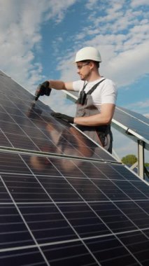 Bir teknisyen güneş panellerini, sistem verimliliğini sağlamak için matkapla tamir ediyor. Açık havada yakalanan bu görüntü, yenilenebilir enerjinin korunması için yapılan çalışmaların altını çiziyor.