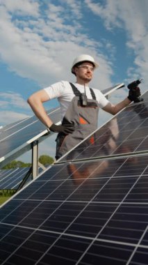 Bir teknisyen bakım için iki güneş paneli dizisi arasında duruyor. Aletleri ve alet çantasını tutarak, güneşli bir günde verimli bir onarım ya da kurulum için hazırlanır.