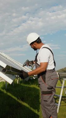 Koruyucu teçhizatla donatılmış Hintli işçiler, büyük bir güneş çiftliğine güneş panelleri kurmak için matkap kullanıyorlar. Onun çabaları yenilenebilir enerji ve çevresel sürdürülebilirliğin ilerlemesine katkıda bulunmaktadır.