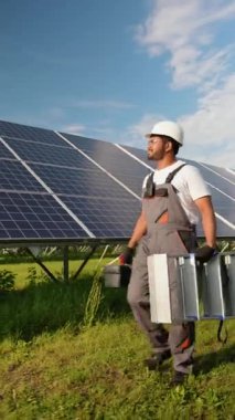 Üniformalı Hintli işçiler güneş çiftliğinde araç ve gereç taşıyarak yürüyorlar. Görüntü, profesyonel çalışma ortamını ve güneş enerjisi sistemlerinin bakımını vurguluyor