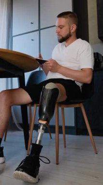 Protez bacaklı bir adam rehabilitasyon sırasında kitap okuyor. Protez bacaklı bir adam masada oturur ve rehabilitasyon sürecinde kitap okur.