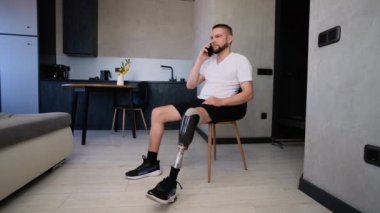 Protez bacaklı bir adam şık dairesinde rahat bir şekilde oturur telefonda konuşurken gülümser. Video, modern bir yaşam alanında neşe, teknoloji ve bağımsızlığı yakalıyor.