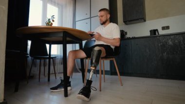 Protez bacaklı bir adam rehabilitasyon sırasında kitap okuyor. Protez bacaklı bir adam masada oturur ve rehabilitasyon sürecinde kitap okur.