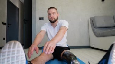 Protez bacaklı bir adam egzersiz ve rehabilitasyon rutininin bir parçası olarak esneme egzersizlerine odaklanır. Aktif kalmaya ve hareket kabiliyetini geliştirmeye kendini adamış