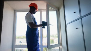 İşçi tulumu ve başlık takan yetenekli bir Afro-Amerikan işçi elektrikli matkap kullanarak pencere kuruyor. O, iş sırasında hassasiyet ve güvenliğe odaklanır.