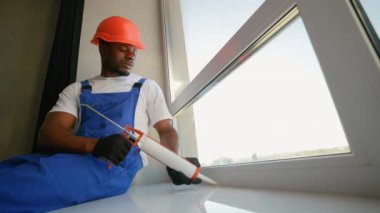 Mavi tulumlu bir inşaat işçisi yeni takılmış bir PVC penceresini yalıtım köpüğüyle kapatıyor. Enerji verimliliği ve hava koruma için uygun mühür sağlanıyor.