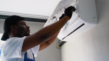 Odaklanmış bir Afrikalı Amerikalı teknisyen, kapalı bir ortamda optimal performans ve temiz hava akışını sağlayan bir klima filtresinin yerini dikkatlice alıyor.