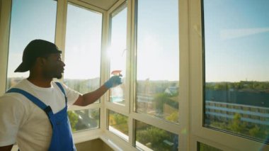Mavi tulumlu ve eldivenli Afro-Amerikalı bir adam balkon camına sprey sıkar ve yıkamaya hazırlanır. Güneş ışığı işini aydınlatıyor, sıcak bir dokunuş ekliyor.
