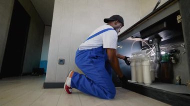 Afro-Amerikalı tesisatçı profesyonel olarak mutfak lavabosunun altına ters osmoz su filtresi yerleştiriyor, temiz ve arıtılmış içme suyu sağlıyor.
