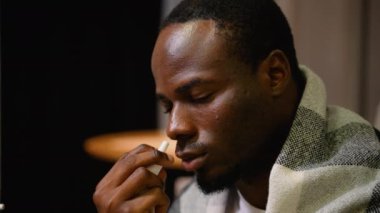 Battaniyeye sarılı olarak burun spreyi sıkan Afro-Amerikalı bir adamın yakın çekimi. Olay yeri, soğuk belirtileri azaltmak için kişisel bakım rutinini yakalıyor.