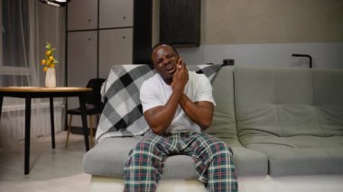 Şiddetli diş ağrısı çeken Afro-Amerikalı bir adam çenesini tutuyor. Onun acı dolu ifadesi rahatsızlığı yansıtıyor, diş sağlığı sorunlarını vurguluyor