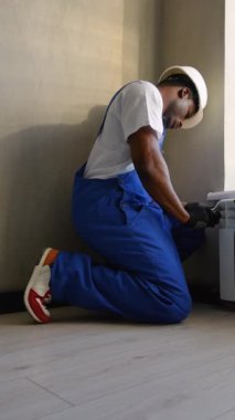 Mavi tulumlu yetenekli teknisyen, ev konforu ve verimliliği sağlamak için geniş bir pencerenin yanına modern bir ısıtma sistemi kuruyor.