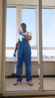 Mavi tulumlu Afro-Amerikan işçiler, bir apartmanın camını temizlemek için cam sileceği bir alet kullanıyorlar, lekesiz ve çizgiden arınmış camları sağlıyorlar.