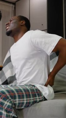 Afrika kökenli Amerikalı bir adam, şiddetli bir rahatsızlıkla boğuşurken belini görünür bir şekilde tutar. İfadesi, şiddetli sırt ağrısını yansıtıyor. Fiziksel hastalıkların etkisini vurguluyor.