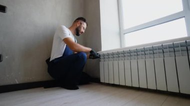 Üniformalı ve eldivenli yetenekli işçiler pencere kenarına radyatör yerleştirir ve modern bir apartman ortamında ideal ısıtma performansı ve enerji verimliliği sağlar.