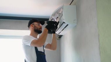 Üniformalı profesyonel teknisyen, bir klimanın bakımını yapıyor. Verimli işlemleri sağlamak ve cihazların ömrünü uzatmak için araçlar kullanıyor.
