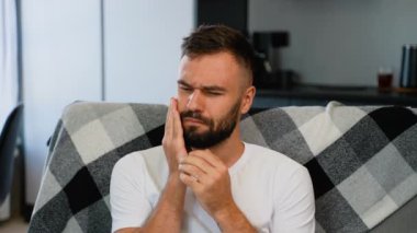 Diş ağrısından muzdarip bir adam yanağını acı içinde tutar, rahatsızlığını dile getirir ve evde rahatlamak ister. Rastgele giyinmiş, rahat bir kanepeye oturuyor.