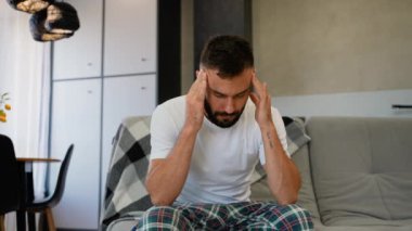 Elleri şakaklarının üzerinde oturan bir adam, gözle görülür şekilde sıkıntılı, baş ağrısı ya da yüksek stres seviyeleri gösteriyor. Görüntü fiziksel ve duygusal rahatsızlığı gösteriyor.