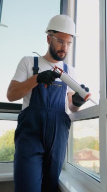 Profesyonel inşaat işçisi pencere kenarlarına köpük macunu sürüyor, yalıtımı artırıyor ve modern yüksek katlı bir apartmanda hava sızıntılarını önlüyor