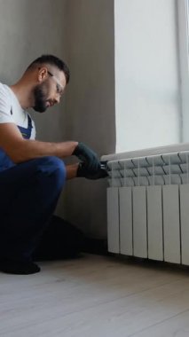 Üniformalı ve eldivenli yetenekli işçiler pencere kenarına radyatör yerleştirir ve modern bir apartman ortamında ideal ısıtma performansı ve enerji verimliliği sağlar.