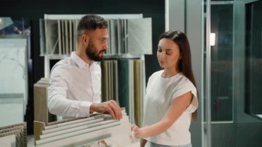 Bir galeri danışmanı kadın müşteriye çeşitli fayans örnekleri sunar ve bilgilendirilmiş bir seçim yapmasına yardımcı olmak için her seçeneğin eşsiz niteliklerini açıklar.