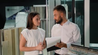 Bir satış danışmanı müşteriye çeşitli tasarım seçeneklerini tartışan ve projesi için en uygun olanı bulmasına yardım eden bir seramik kataloğu sunar. Etkileşim odaklı ve profesyonelce.