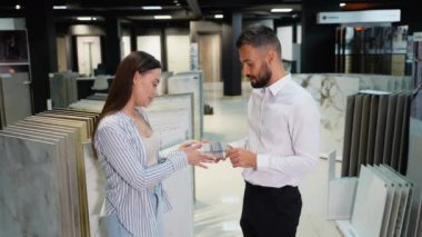 Sergi salonundaki bir kadın müşteri ve bir satış danışmanı arasında dostça bir etkileşim. Danışman fayans seçeneklerini açıklıyor, projesi için bilinçli bir seçim yapmasına yardım ediyor.