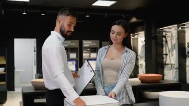 Bir satış danışmanı, mağazada bir bayan müşteriyle modern bir lavaboyu tartışıyor. Harika bir fiyata mükemmel bir fikstür bulmak için özel bir indirimi vurguluyor.