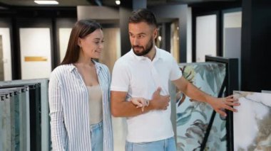 Yeni evli bir çift, yeni evlerinin dekorasyonunu geliştirmek için çeşitli fayans seçeneklerini inceleyerek sergi salonunda yürür.