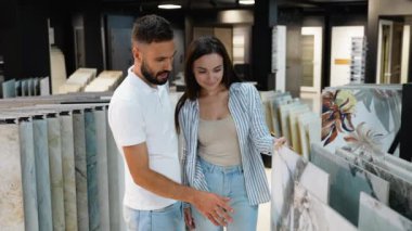 Bir çift mağazada çeşitli fayans seçeneklerini inceliyor, ev dekorasyonu projeleri için mükemmel bir eşleşme bulmak için stil ve renkleri dikkatlice inceliyor.