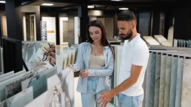 Genç bir çift, bir mağazadaki fayans örneklerini inceliyor ve ev yenileme projesi için vizyonlarına uygun mükemmel bir tasarım seçiyor.