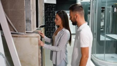 Genç bir çift, banyo tadilatları için fayans tasarımlarını dikkatlice seçerken, mağazadaki çeşitli stil ve dokuları incelerken görülüyor.