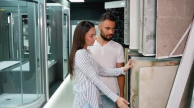 Genç bir çift, banyo tadilatları için fayans tasarımlarını dikkatlice seçerken, mağazadaki çeşitli stil ve dokuları incelerken görülüyor.