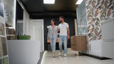 Bir çift banyo dekorunu ve mobilyaları inceliyor, çeşitli stillerle dolu bir galeriye bakıyor ve yenileme projelerine ilham vermek için bitiriyor.