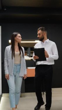 Bir satış danışmanı müşteriye fayans galerisindeki banyo dekorasyonu seçeneklerinde rehberlik eder, banyo tasarımını geliştirmek için şık fayanslar ve fikstür kombinasyonlarını vurgular.