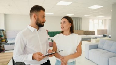 Bilge bir mobilya danışmanı, modern bir sergi salonunda stil, konfor ve işlevsellik konusunda rehberlik ederek ideal kanepeyi seçen müşteriye yardımcı olur.